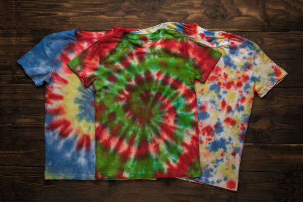 istock Three bright tie dye T-shirts on a wooden background. 2149911432