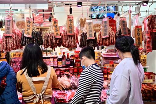 Nanmen market (Publicly accessible), TW-01.18.24: Liver sausage and Chinese sausage: Lunar New Year staples in Chinese-speaking areas, made beforehand and savored during celebrations. They're made by marinating, drying, or smoking meat. A vendor enthusiastically introduces products to a customer while nearby customers browse the merchandise.