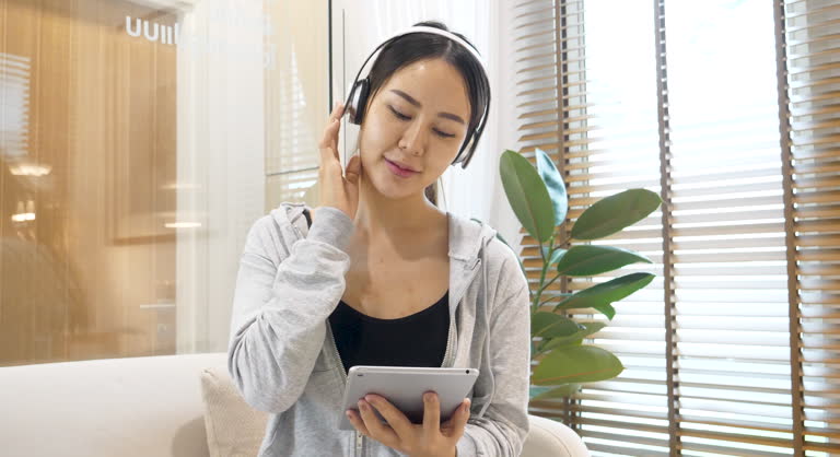 Happy Woman hands using smartphone use headphones listen to music. digital technology tablet asian woman surfing internet online website. Female asian sitting couch sofa video call conference at home