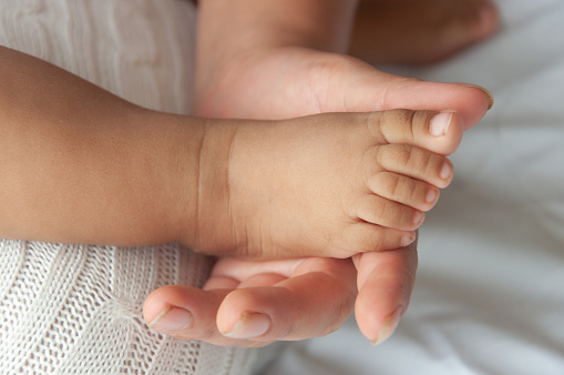 A tender moment as a newborns tiny feet are cradled by an adults hand, symbolizing care and love.