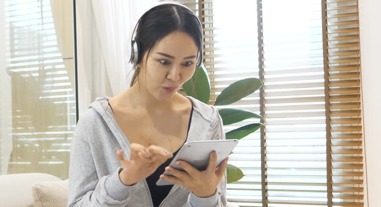 Happy Woman hands using smartphone use headphones listen to music. digital technology tablet asian woman surfing internet online website. Female asian sitting couch sofa video call conference at home