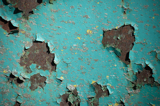 Turquoise paint chips and peels away, it reveals the darker rusted metal beneath, contrasting the once vibrant paint with the corroded surface