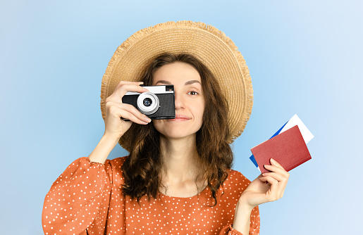 happy female tourist with camera and passport with tickets in hands on blue background