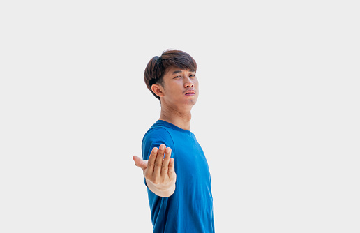 A young Asian man in his 20s wearing a blue t-shirt makes wave your hands to your opponent or make a fighting pose isolated on a gray background. Finding a fight or fighting with an enemy or opponent