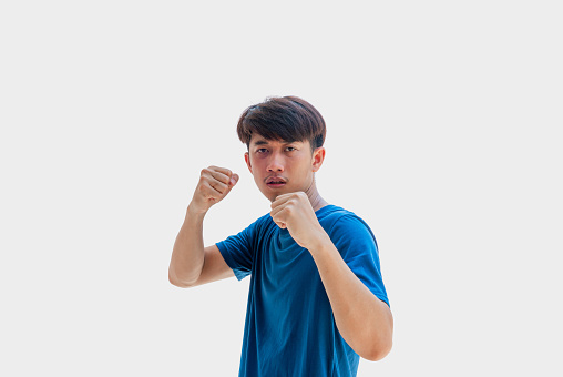 A young Asian man in his 20s wearing a blue t-shirt makes pretend to set up your guard in order to punch isolated on a gray background.