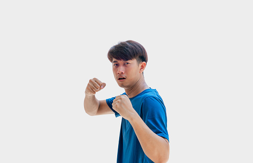 A young Asian man in his 20s wearing a blue t-shirt makes pretend to set up your guard in order to punch isolated on a gray background.