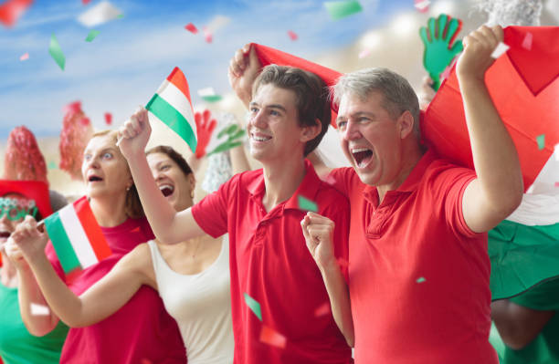Hungary football supporter on stadium. Hungarian fans on soccer pitch watching team play. Group of supporters with flag and national jersey cheering for Hungary. Championship game.