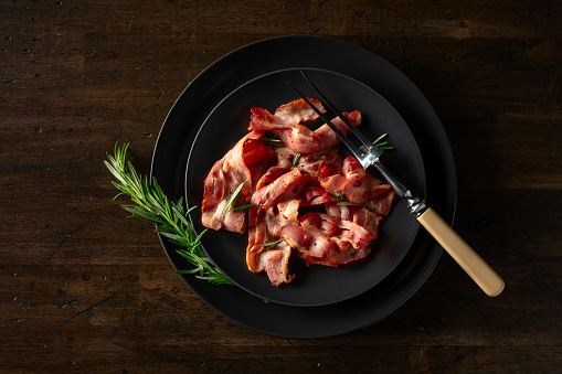 Roasted bacon slices with rosemary on an  old wooden table. Copy space. Top view.