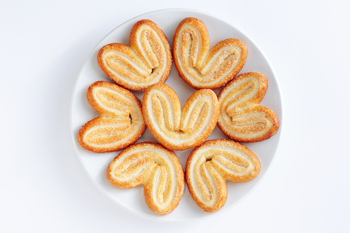 Palmier, also as elephant ears, a traditional French pastry in a plate on a white background, top view