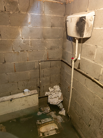 Dirty toilet room with pile of used toilet paper in the corner, uncoated concrete flooring and cinder brick walls. Developing country poorness.