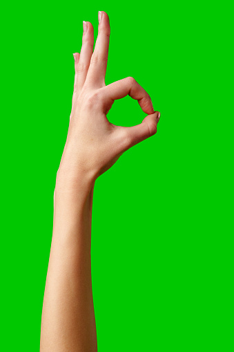 A solitary hand is raised against a bright green background, fingers curled into a circle while the thumb and index finger touch to form the universally recognized okay sign, suggesting approval or that everything is fine.