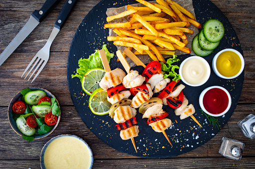 Shashlik - grilled meat and French fries on stone plate on black wooden table