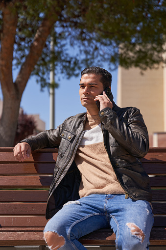 Handsome man talking on the phone while sitting on a bench