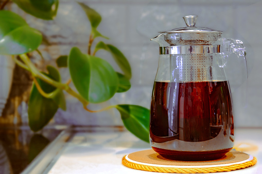 A glass teapot with brewed black tea is in the kitchen, close-up.
