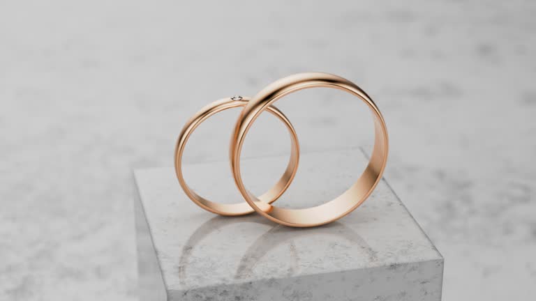 Camera rotates around two gold wedding rings. Two gold wedding rings stand on a stone, concrete podium.