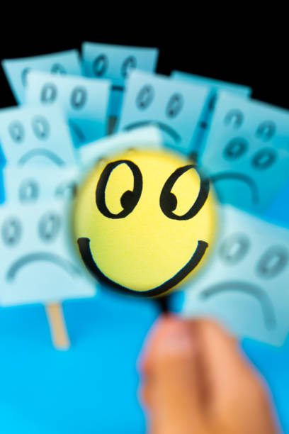 Sticky note with hand drawn Smiley face looked through the magnifying glass with Sad faces in background. Positive way of thinking overcomes negative