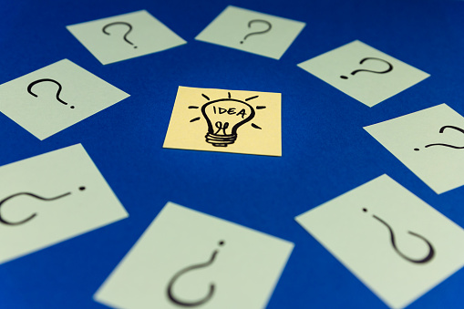 Light bulb surrounded by Question marks drawn on sticky notes. Idea, inspiration and creative thinking concept