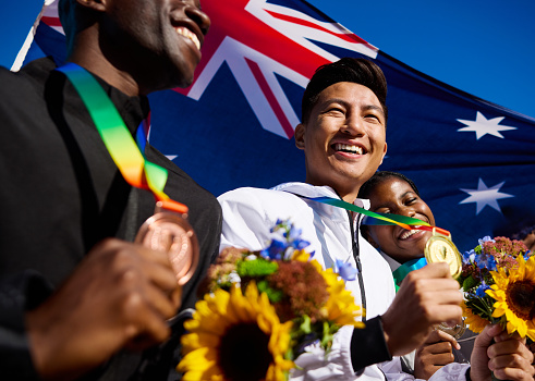 Ecstatic Australian athletes with medals and bouquets against the Australian flag. Joyful group celebration portrait. Team spirit and international unity concept.