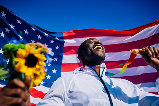 Exuberant athlete standing on the podium with an American flag in the background. International sports event concept outdoor portrait.