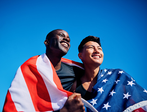 Two International athletes wrapped in American flags looking forward with optimism. Unity and teamwork concept outdoor portrait. Patriotic pride and friendship theme.