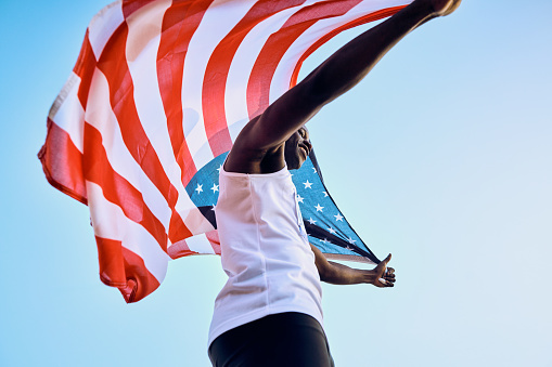 Triumphant Team USA athlete raising American flag high. Outdoor portrait with clear sky. Freedom and victory concept.