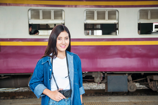 Portrait young asian traveller woman smiling sitting railway station look at camera. Beautiful women tourist relaxing using camera hold on digital tablet while waiting train departure enjoy holiday