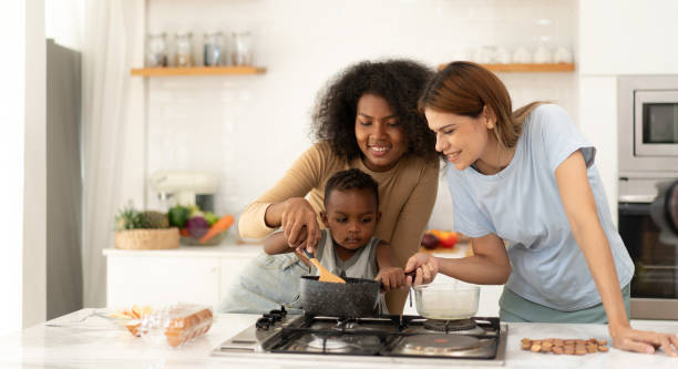 istock Multiracial lesbian and married girlfriend standing together at kitchen counter playing with their biracial son. 2149938860