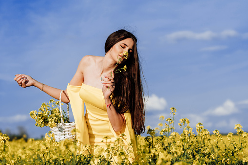 Lovely young woman in yellow dress standing in a sunny field full of yellow canola