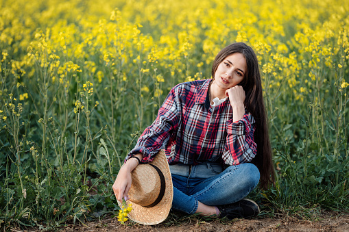 Portrait of a beautiful young woman in a straw hat in a rapeseed field