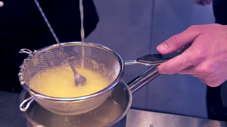 Slow motion 100fps footage of bartender pouring lemon juice in a colander and stirring with a spoon.Tight close up shot