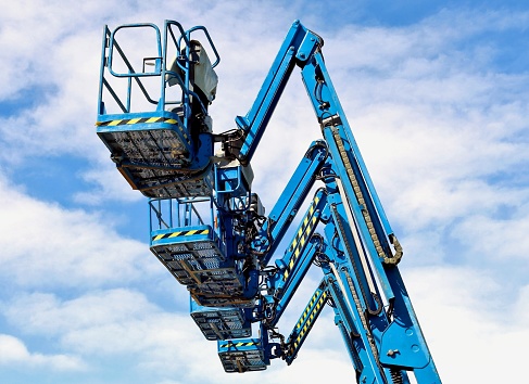 Blue aerial work platforms of cherry pickers in a row against blue sky with clouds