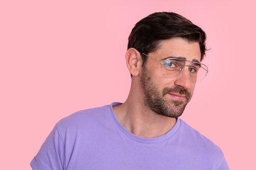 Adult man wearing glasses and a purple shirt, smiling subtly against a plain pink background with copy space