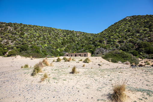 old abandoned building, without windows and doors, ruins on the beach, hill in the background, sardinia, italy