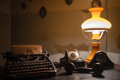 Retro typewriter, rotary phone and lamp on the antique desk table background. Writer or detective table concept background.