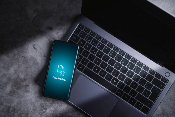 istock Smartphone laying on laptop while downloading files or installing software on phone. 2149953847