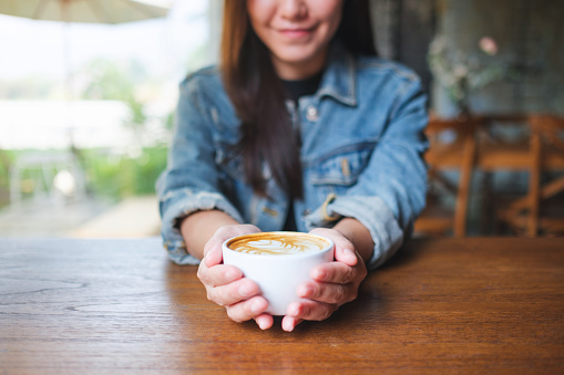Closeup image of a young woman holding a cup of latte coffee