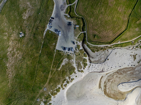 Aerial view of a beachside campground positioned between rich grasslands and a sandy beach.  The campground presents clear patterns in the sand, indicating the tide has recently receded. Several vehicles and campers are parked, indicating the they're having a stop over.