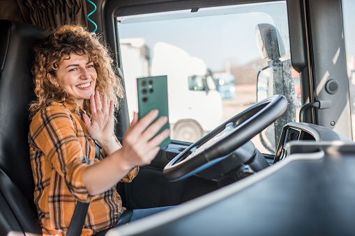 A professional female truck driver uses a smartphone in the truck cabin during a break