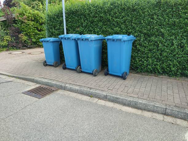 istock Three large and one small blue plastic garbage cans stands on the side of the road in front of a green hedge ready for collection 2149965341