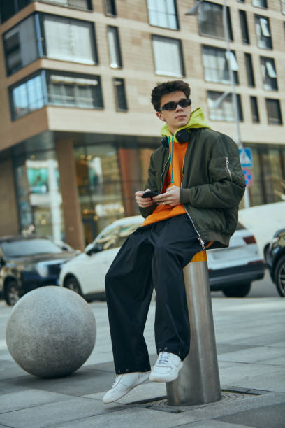istock Fashion-forward young male model posing in oversized neon attire that emphasize his urban flair against city's dynamic backdrop 2149967737