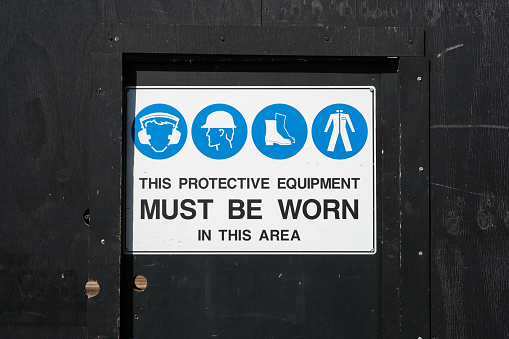 Protective equipment requirements sign on a black wooden door.