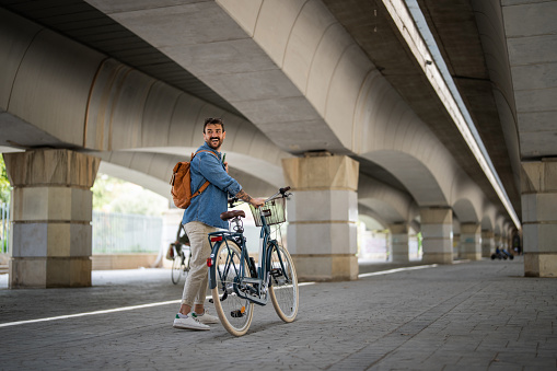 Full length of modern male in casual outfit pushing his bicycle