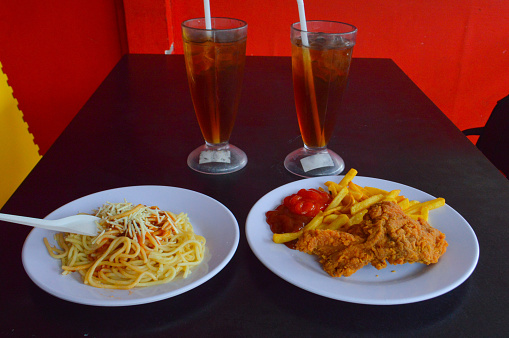 Simple Fast Food Meal Of Fried Chicken, French Fries, Spaghetti, With Two Glasses Of Iced Tea On The Dining Table Of The Eatery