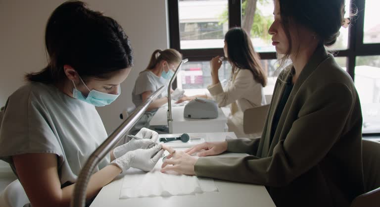 Manicurist treats the cuticles of the client with an electric manicure device.