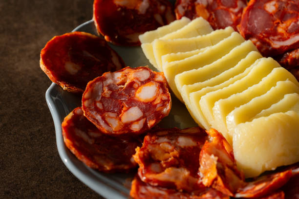 A traditional Alentejo sausage, known as paio, sliced and displayed alongside a rustic cheese wheel on a white plate in a charming restaurant setting.