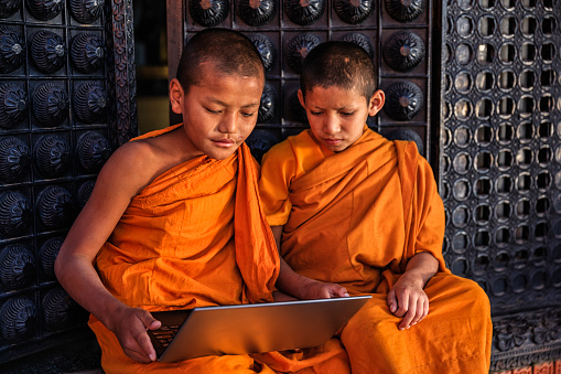 Novice Buddhist monks using laptop in the monastery in Bhaktapur, Nepal. Bhaktapur is an ancient Newar town in the east corner of the Kathmandu Valley, Nepal. It is the third largest city in Kathmandu valley and was once the capital of Nepal during the great Malla Kingdom until the second half of the 15th century. Bhaktapur is listed as a World Heritage by UNESCO for its rich culture, temples, and wood, metal and stone artwork.