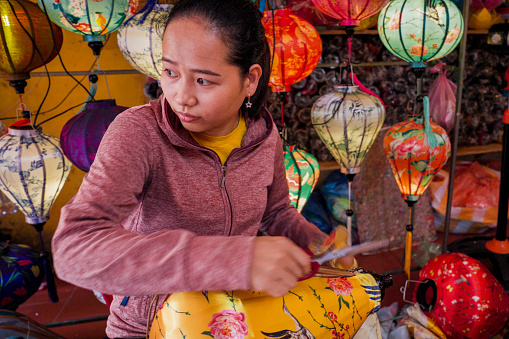 Vietnamese woman making traditional silk hanging lanterns, night market in Hoi An. Hoi An is situated on the east coast of Vietnam. Its old town is a UNESCO World Heritage Site because of its historical buildings.