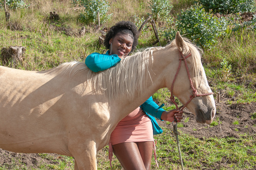 A woman shares a tender moment with a palomino horse, against a backdrop of verdant hills.
