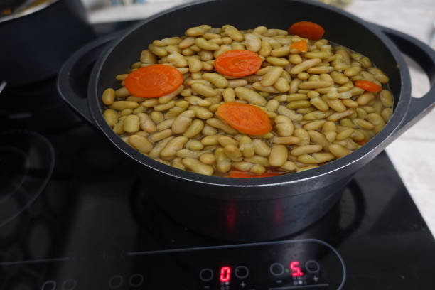 Flageolets and carrots being cooked in a casserole dish on a ceramic hob