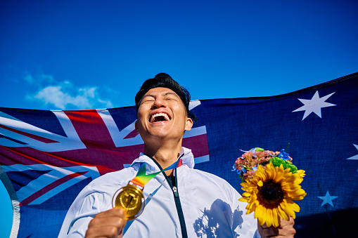 Ecstatic athlete with medal and sunflower bouquet against Australian flag. Joyful victory celebration outdoor portrait. National pride and achievement concept.